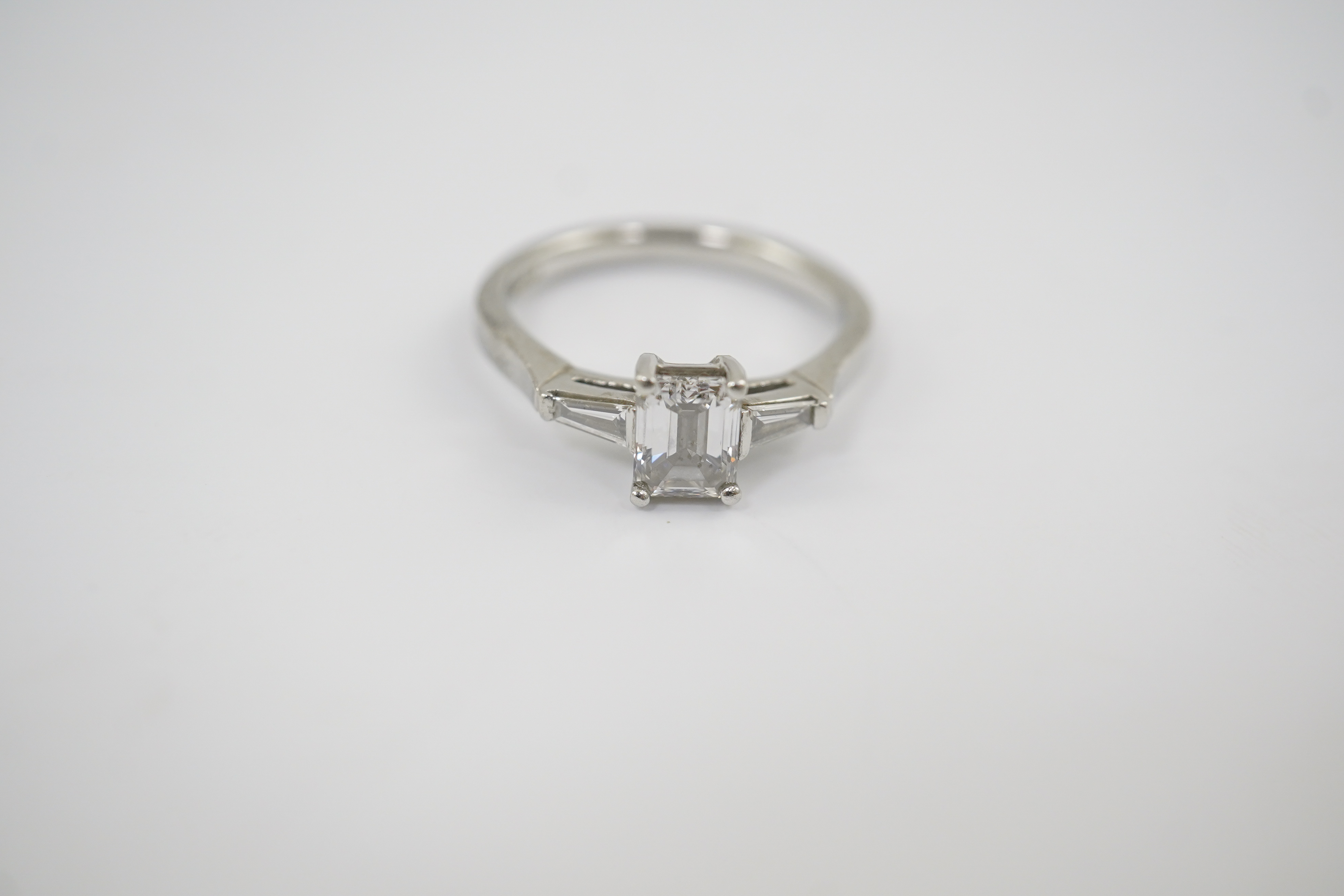 A modern platinum and single stone emerald cut diamond set ring, with two stone tapered baguette cut diamond set shoulders